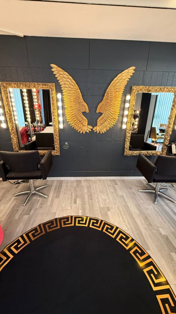 Zwei elegante Friseurstühle vor einem Spiegel mit goldenen Flügeln an der Wand