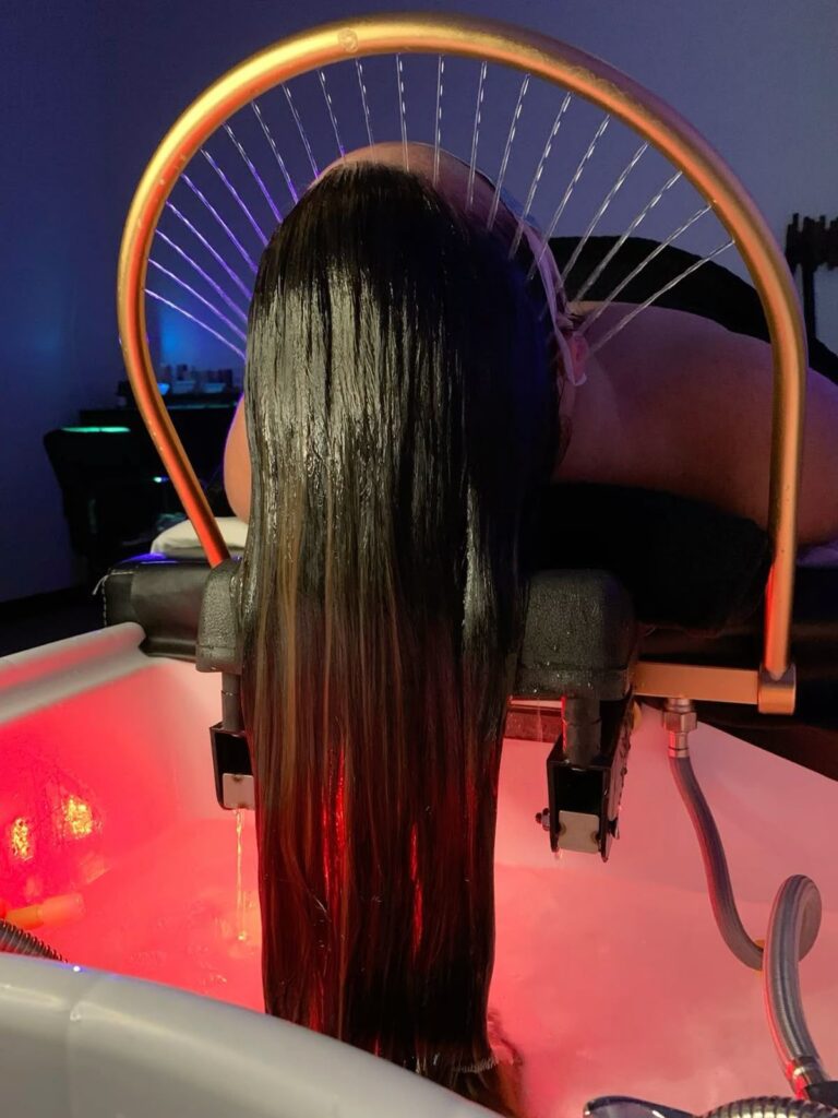 Eine Frau liegt entspannt mit nassen langen braunen Haaren über einer LED-beleuchteten Haarwaschstation